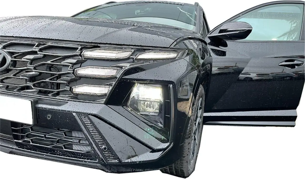 Vue avant droite rapprochée du Hyundai Tucson 2025 noir brillant avec porte ouverte et phares allumés sous la pluie.