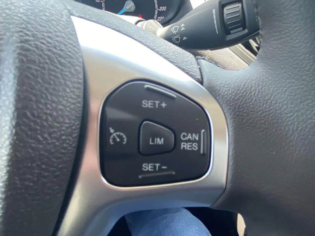 Gros plan sur les commandes du régulateur de vitesse au volant cuir noir du Ford Tourneo Courier blanc, version 2022.