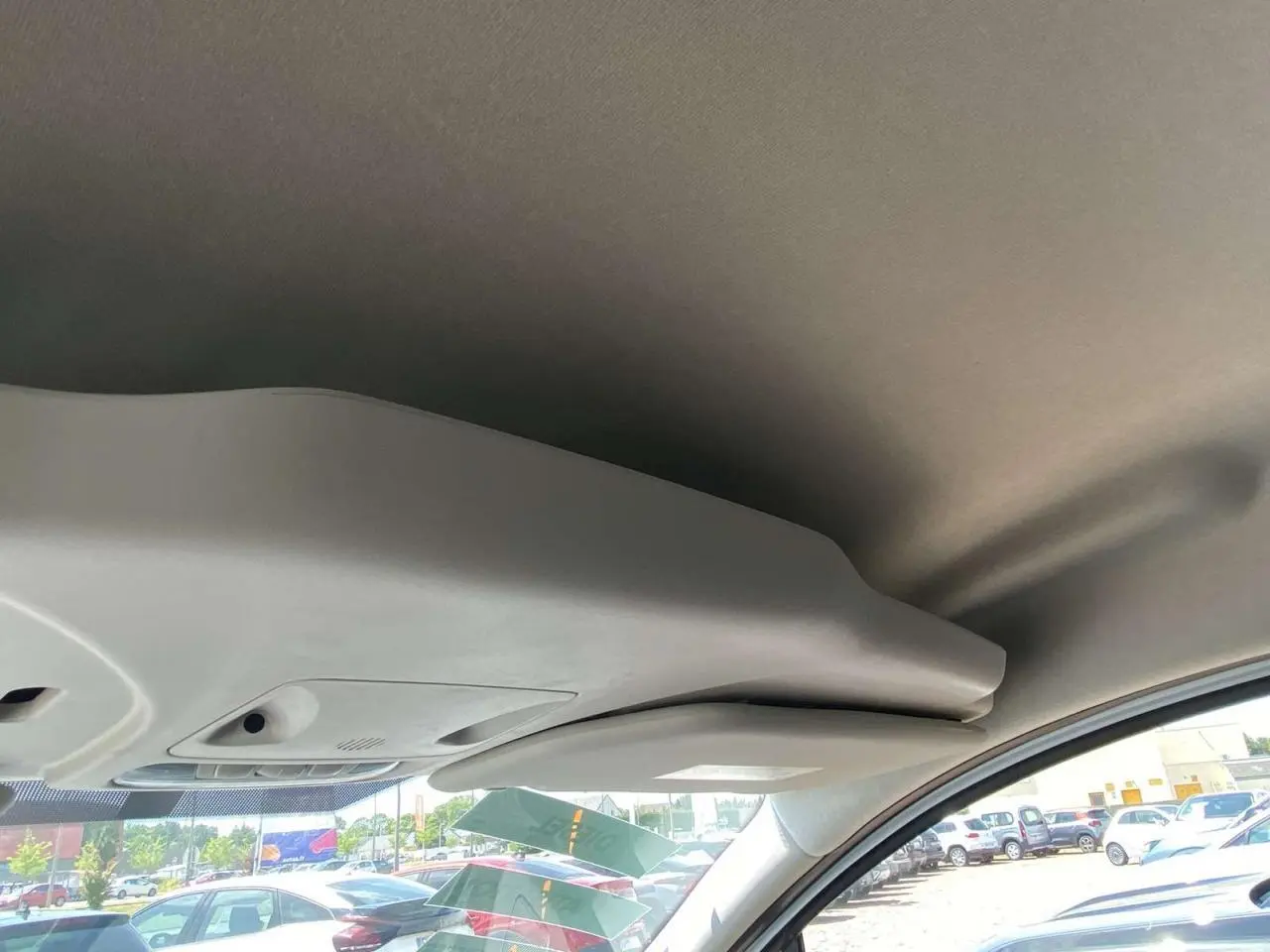 Vue intérieure du toit et pare-soleil côté conducteur d'un Ford Tourneo Courier blanc, avec vue partielle sur le pare-brise et le parking extérieur.