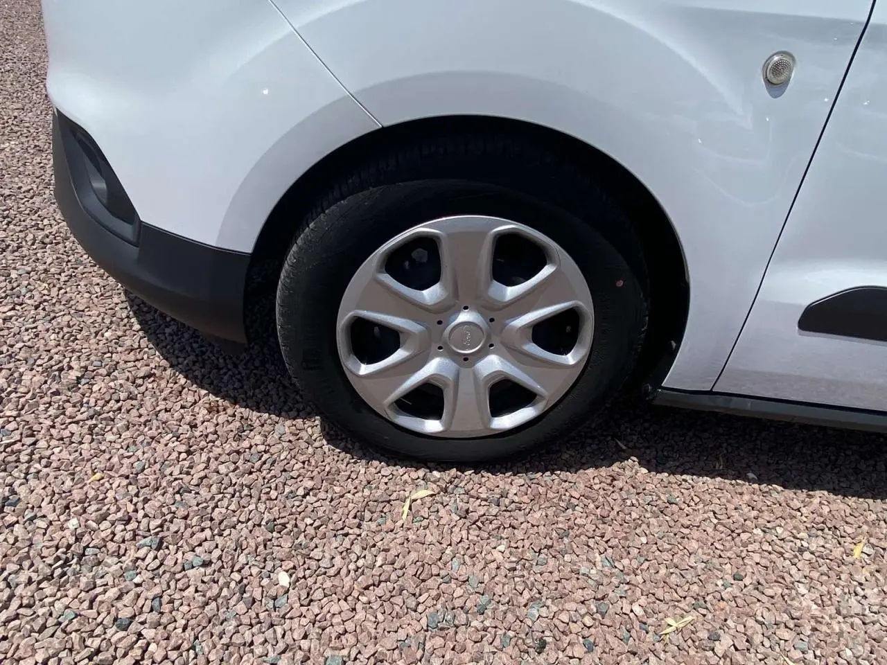 Gros plan sur la roue avant droite avec enjoliveur argenté du Ford Tourneo Courier blanc, sur sol en gravier.