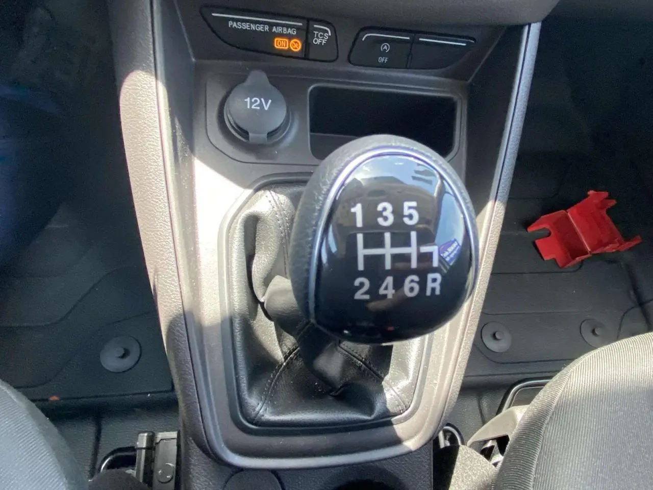 Gros plan sur le pommeau de levier de vitesses manuel noir du Ford Tourneo Courier blanc, avec prise 12V en arrière-plan.