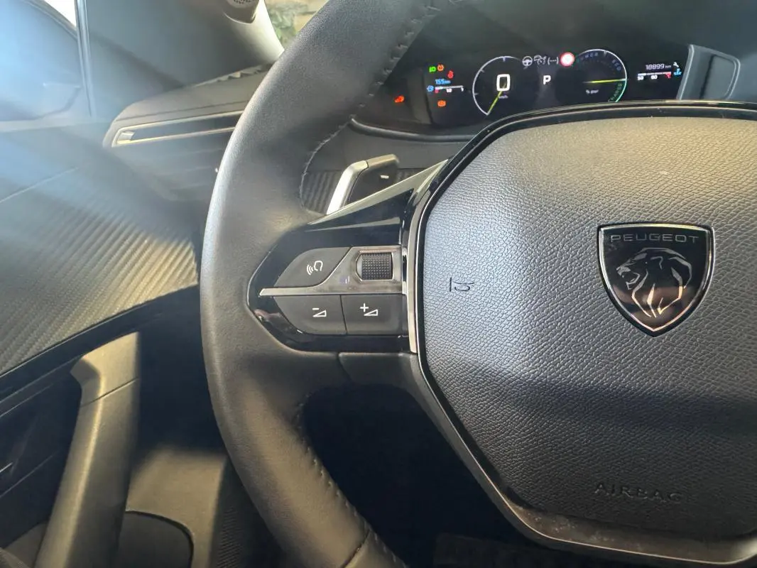 Vue rapprochée du volant cuir noir avec logo Peugeot et tableau de bord numérique allumé du 2008 Hybrid 145 Allure.