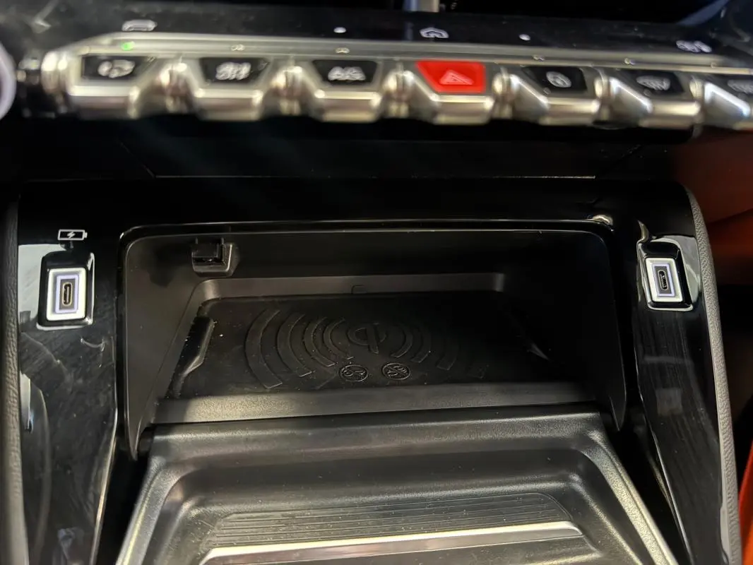 Gros plan sur la console centrale noire du Peugeot 2008 Hybrid 145, avec zone de charge sans fil et ports USB-C.