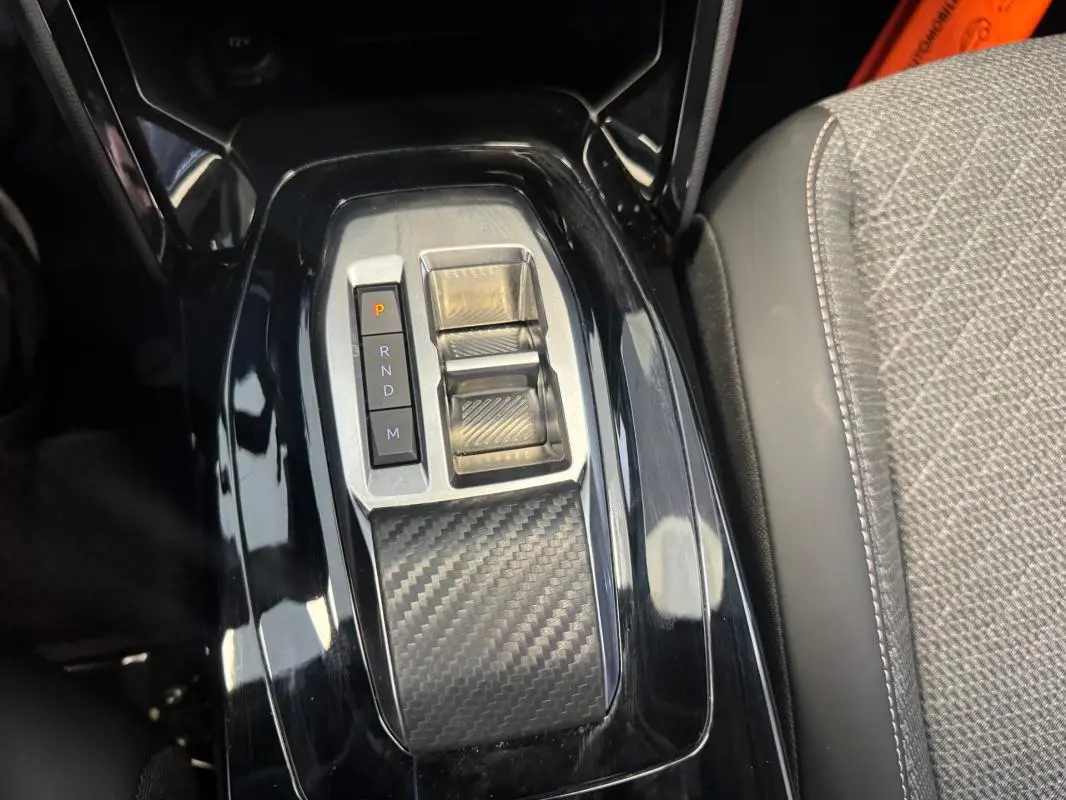 Gros plan sur la console centrale noire brillante avec commandes de boîte auto et accoudoir tissu gris du Peugeot 2008 Hybrid 145.