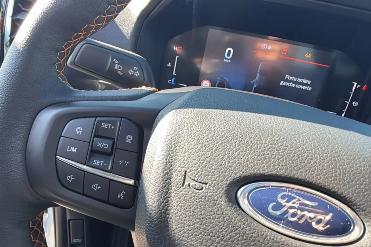 Gros plan sur le volant cuir noir avec surpiqûres orange et commandes multifonctions du Ford Ranger Wildtrak 2025.