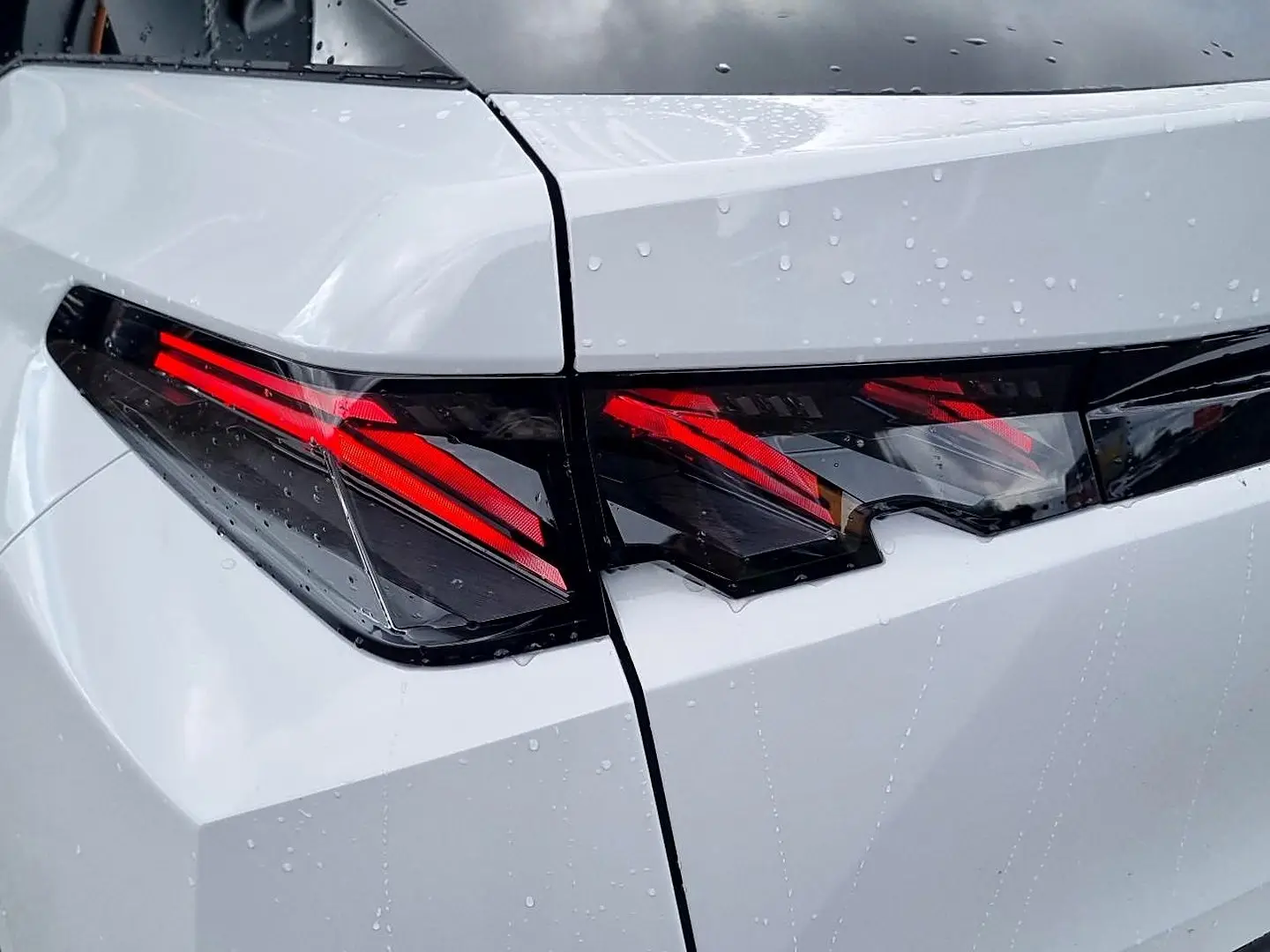 Gros plan sur les feux arrière LED rouges du Peugeot 3008 blanc avec toit noir, vue arrière côté gauche sous la pluie.