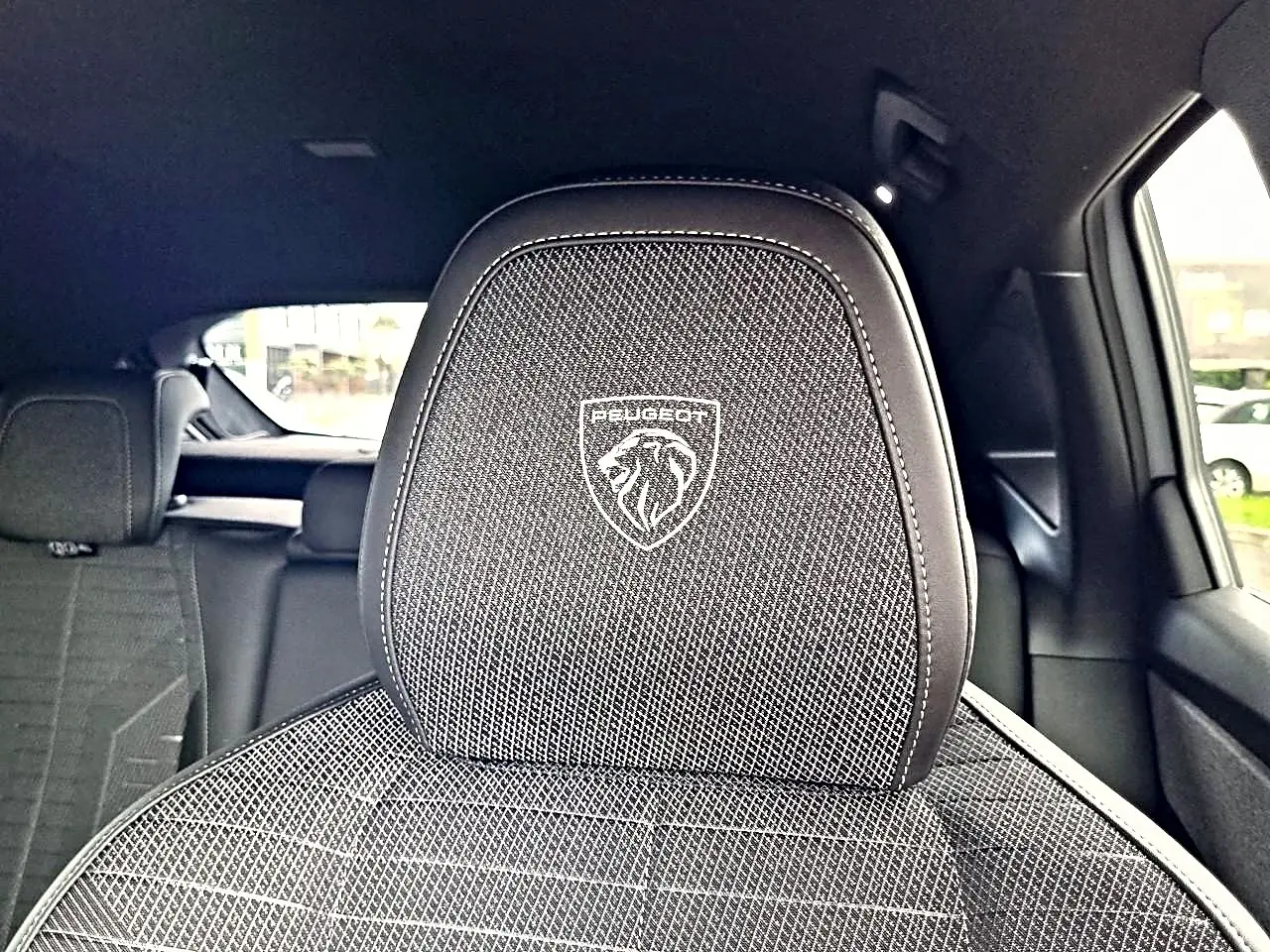 Gros plan sur l'appui-tête avant noir avec logo Peugeot, intérieur tissu et cuir du SUV 3008 blanc toit noir.