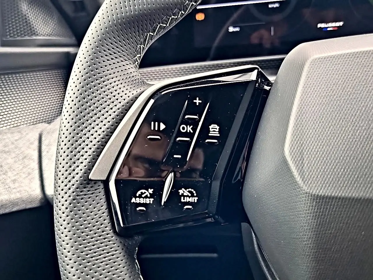 Gros plan sur la commande gauche du volant cuir perforé du Peugeot 3008 blanc toit noir, avec boutons multifonctions.
