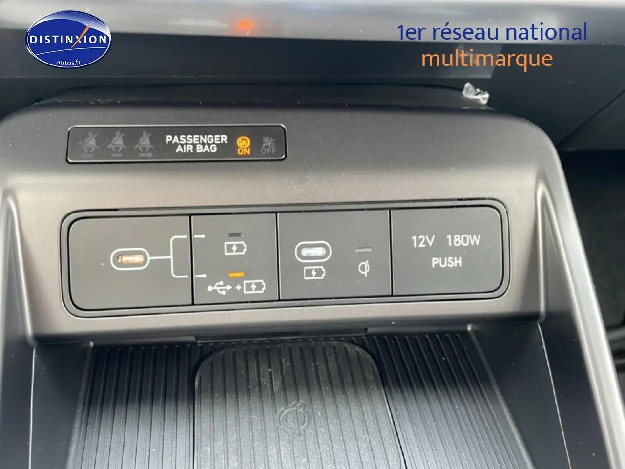 Vue rapprochée du panneau de commandes USB, prise 12V et indication airbag passager du Hyundai Kona bleu 2025.