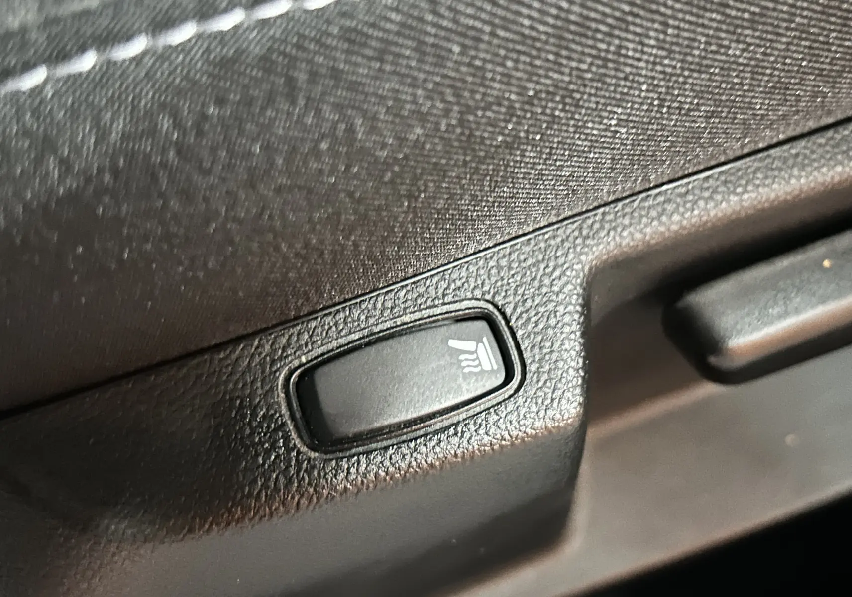 Gros plan sur le bouton de siège chauffant en plastique noir dans l'habitacle du Dacia Duster blanc 2023.