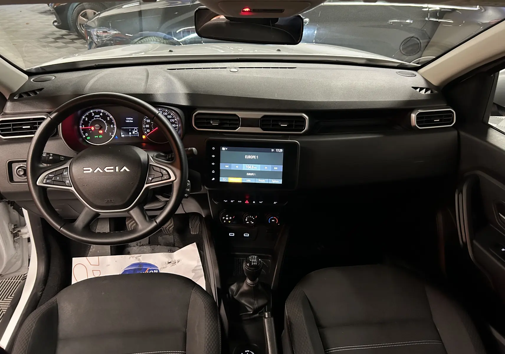 Vue intérieure avant du Dacia Duster blanc 2023, tableau de bord avec écran tactile et volant multifonction.