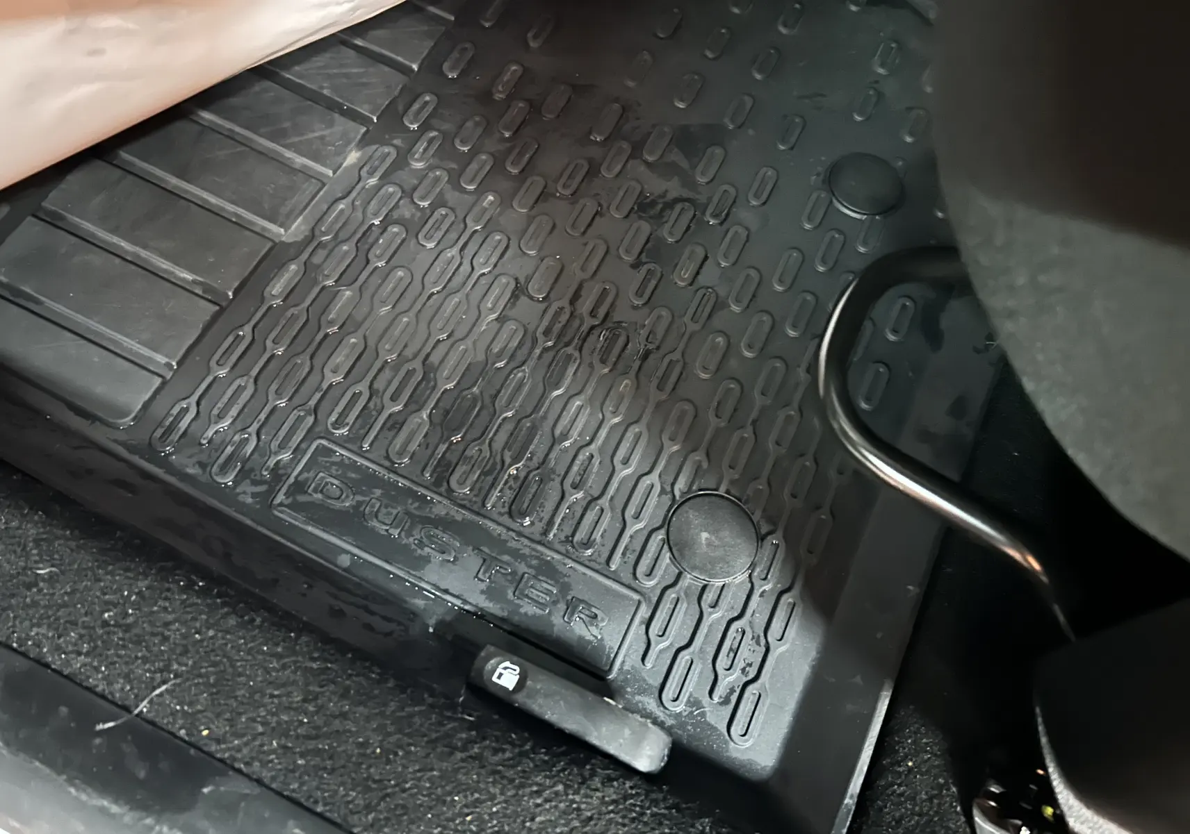 Gros plan sur le tapis de sol noir côté conducteur du Dacia Duster avec logo embossé visible.
