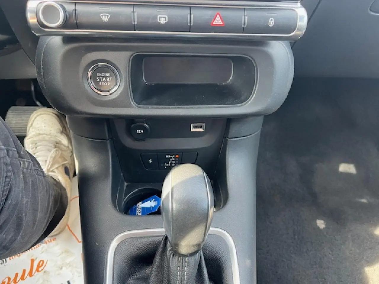 Vue intérieure centrée sur la console centrale d'une Citroën C3 noire 2023, avec levier de boîte auto et bouton start/stop visible.