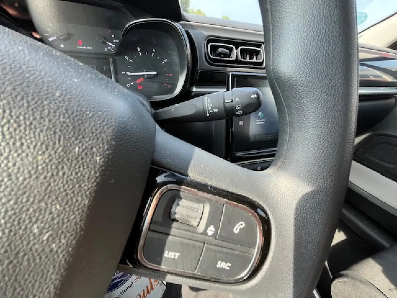Gros plan sur le volant noir de la Citroën C3 2023, avec commandes audio intégrées et tableau de bord en arrière-plan.