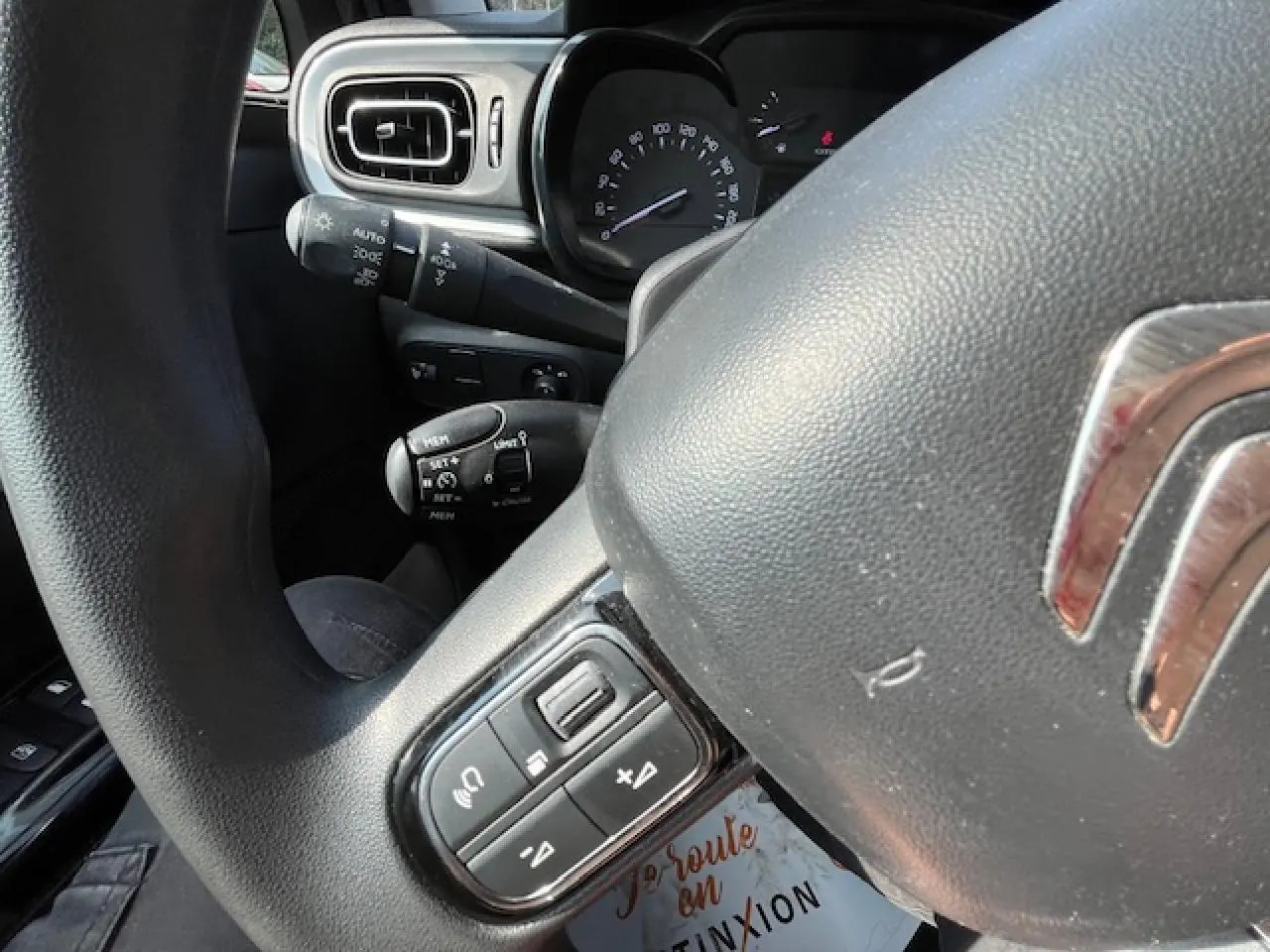 Gros plan sur le volant noir de la Citroën C3 2023 avec commandes audio et tableau de bord en arrière-plan.