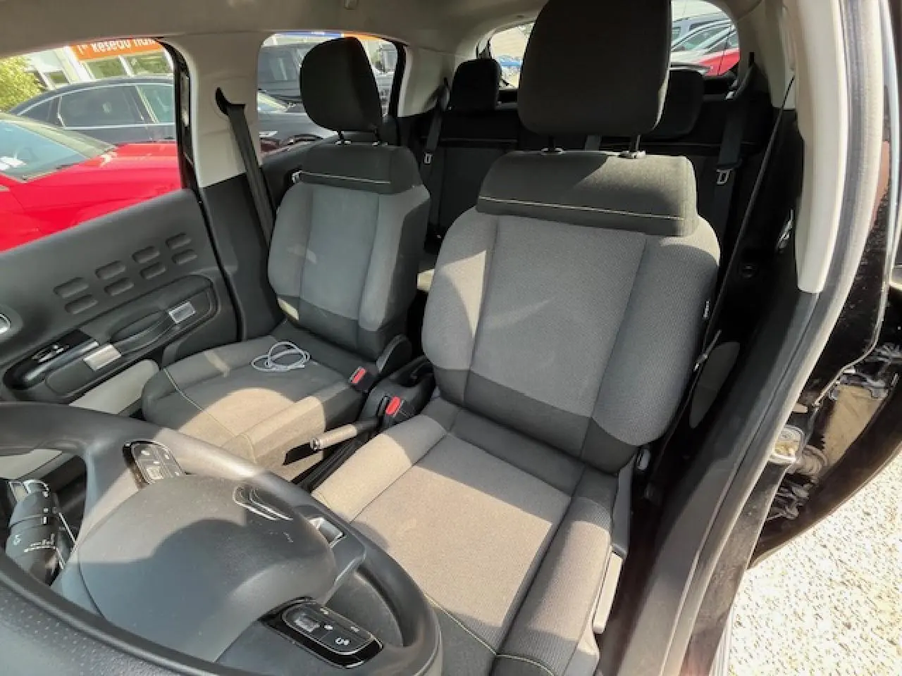 Vue intérieure côté conducteur de la Citroën C3 noire 2023, montrant les sièges tissu gris et le volant multifonction.