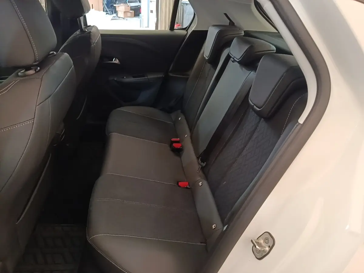 Vue intérieure côté arrière droit de l’Opel Corsa blanc, montrant la banquette arrière noire avec appuie-têtes et ceintures de sécurité rouges.