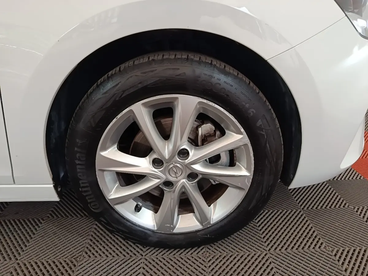 Gros plan sur la roue avant droite d’une Opel Corsa blanche 2022 avec jante alliage et logo Opel visible.
