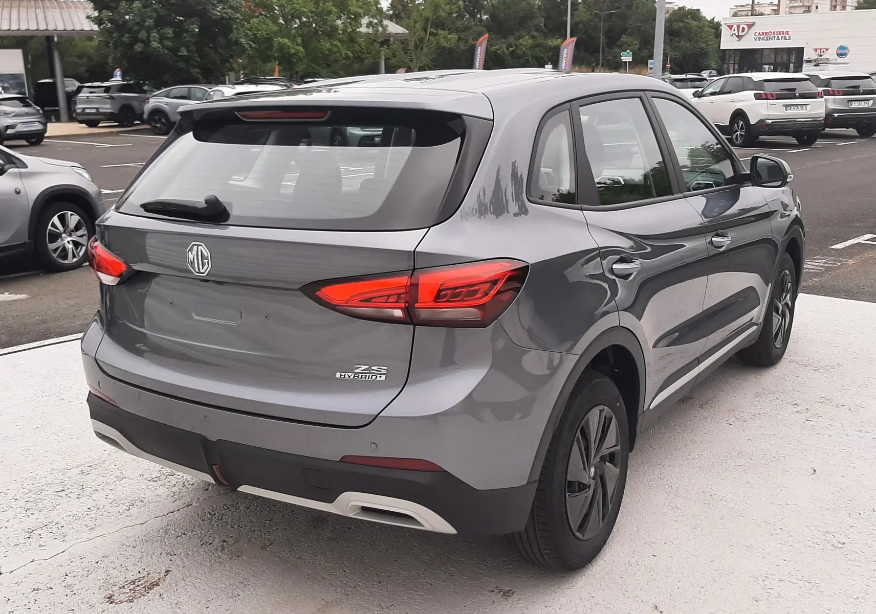 Vue 3/4 arrière droite d'un MG ZS Camden Grey hybride essence 2026 avec feux arrière LED et jantes noires.
