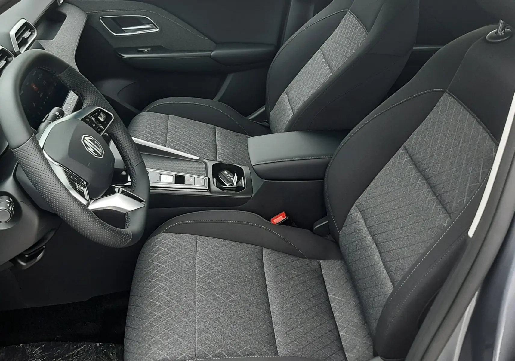 Vue intérieure côté conducteur du MG ZS 1.5 Hybrid+ 2026 en Camden Grey, sièges tissu gris avec surpiqûres et volant multifonction.