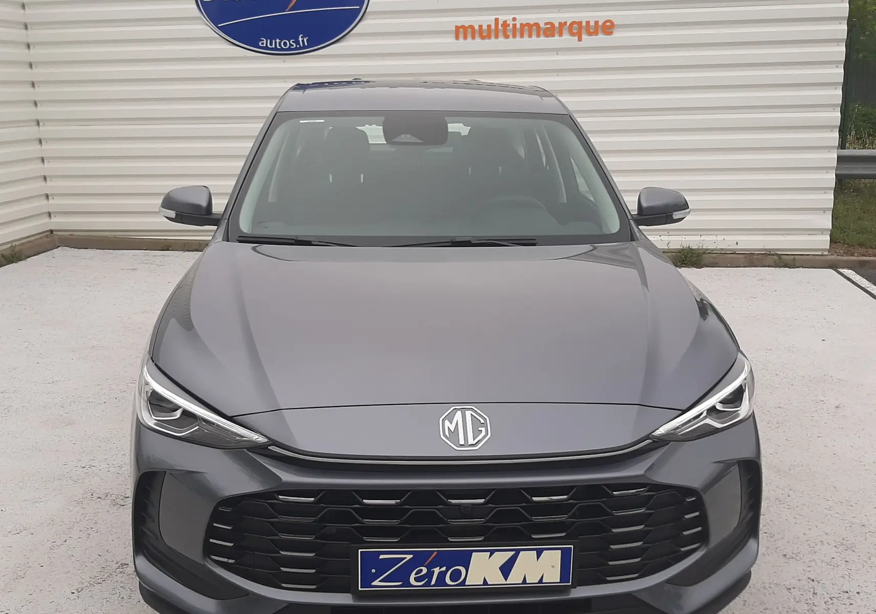 Vue frontale d'un MG MOTOR ZS 1.5 HYBRID+ 197CH en Camden Grey, avec calandre noire et logo MG visible.