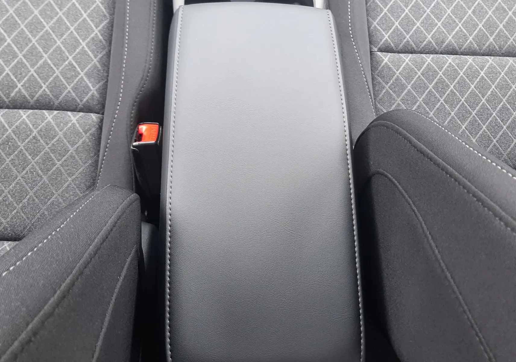 Vue plongeante sur l'accoudoir central en cuir noir entre les sièges tissu gris à motifs du MG ZS 1.5 Hybrid+ 2026.