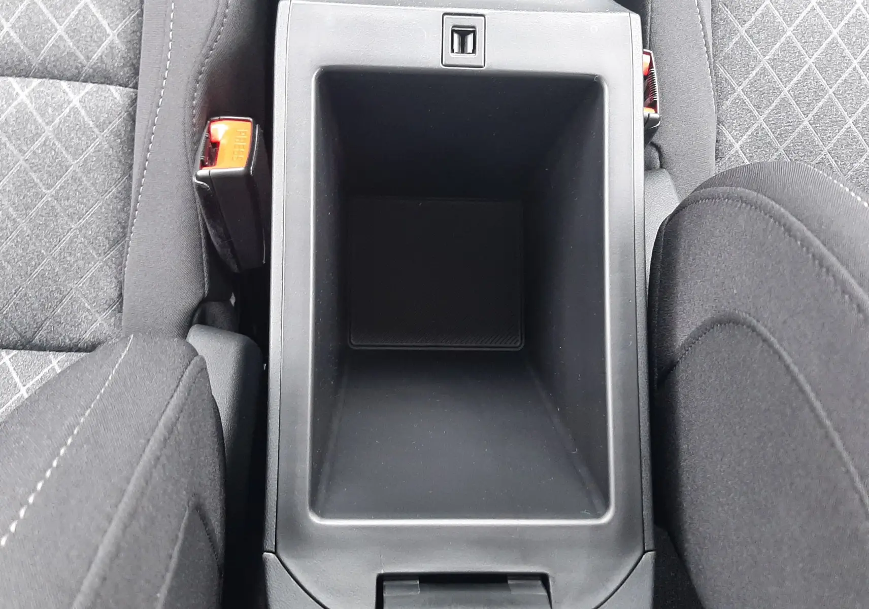 Vue plongeante sur le rangement central noir entre les sièges avant en tissu gris à motifs du MG MOTOR ZS hybride 2026.