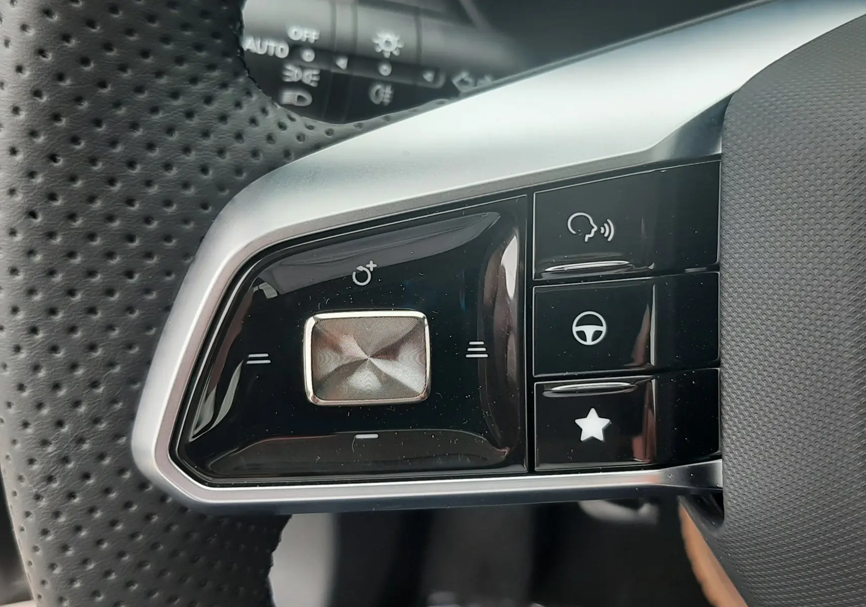 Gros plan sur les commandes gauche du volant perforé noir du MG ZS Camden Grey 2026, avec boutons multifonctions et finition argentée.