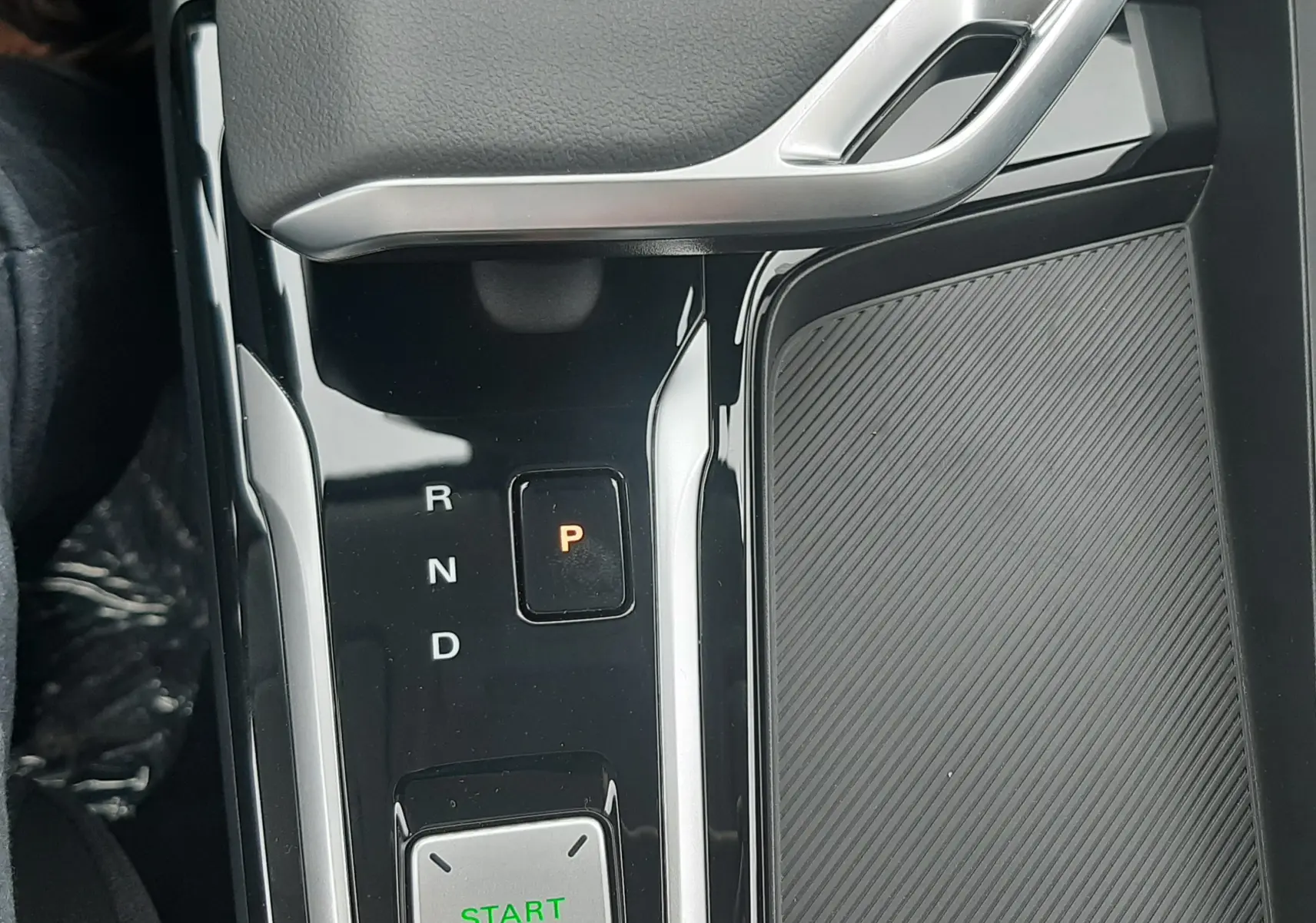 Gros plan sur la console centrale noire brillante du MG ZS hybride 2026, avec levier de vitesses automatique et bouton start/stop vert.