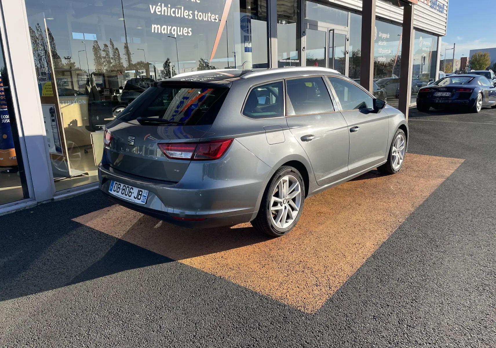SEAT LEON ST gris vue 3/4 arrière droit, garée devant un showroom avec reflets sur la carrosserie.