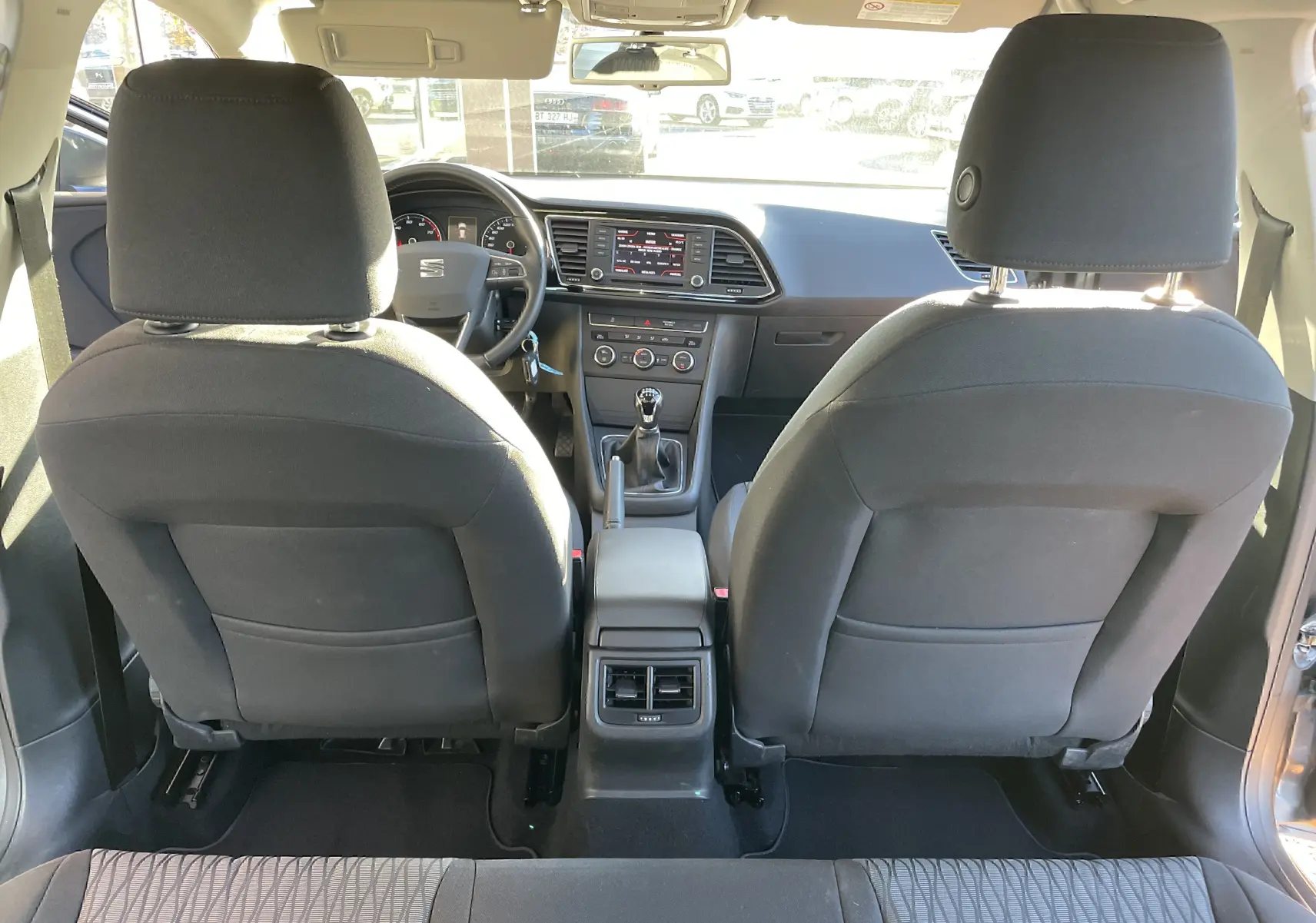 Vue intérieure arrière d'une SEAT LEON ST gris 2013, montrant les sièges avant en tissu noir et la console centrale avec boîte manuelle.