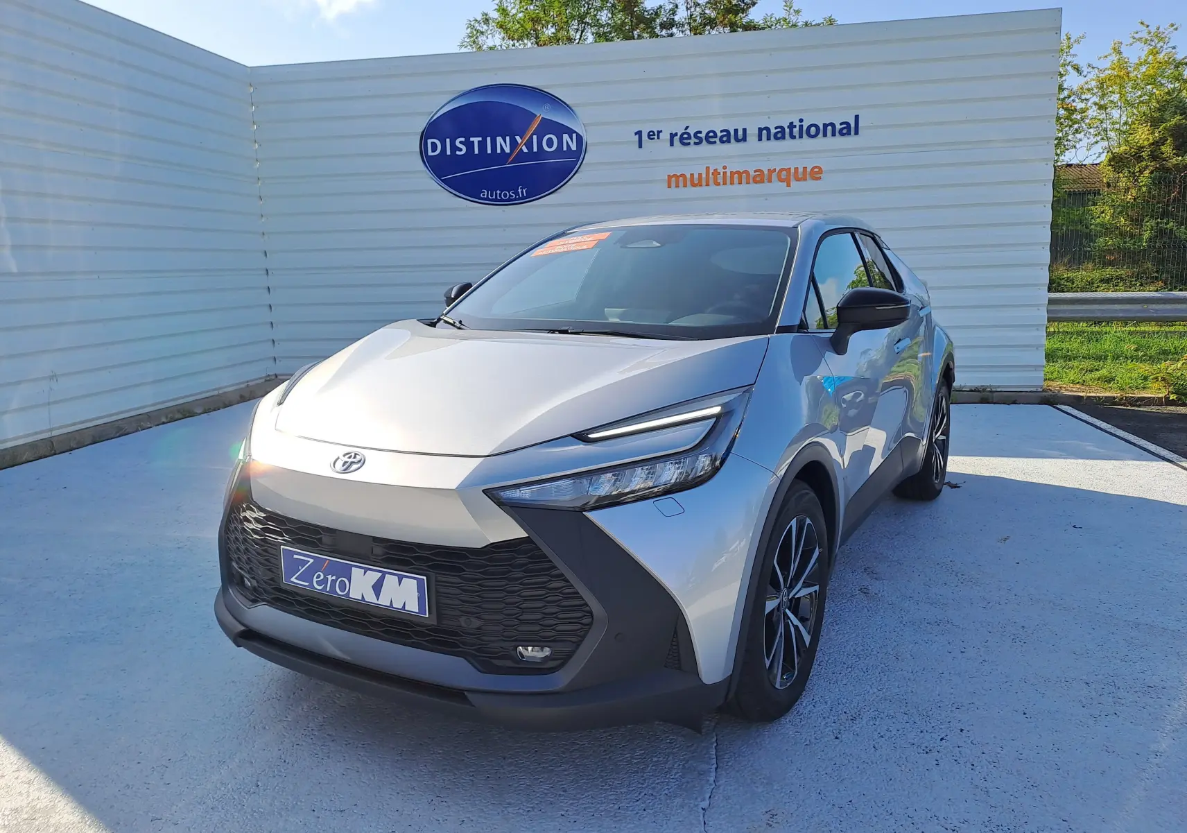 Toyota C-HR gris minéral en 3/4 avant droit, avec calandre noire et jantes bi-ton 18 pouces visibles.