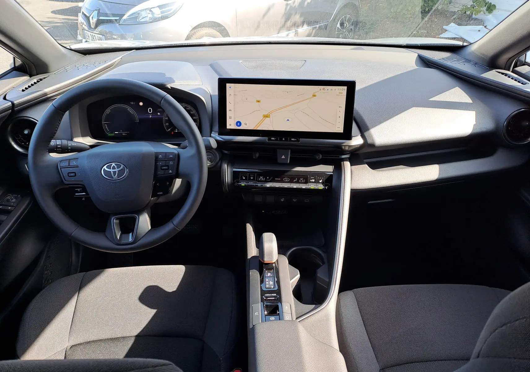 Vue plongeante sur l'intérieur du Toyota C-HR gris minéral, montrant la console centrale et les sièges avant en tissu noir.