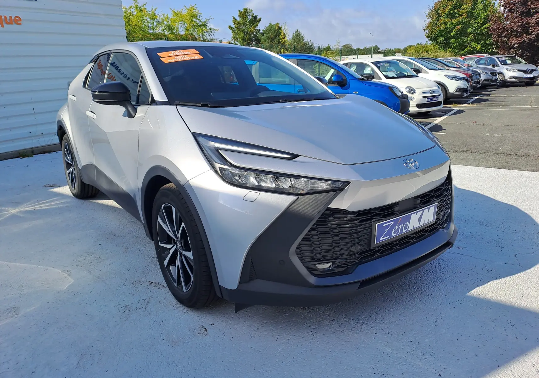 Toyota C-HR II Style 1.8 Hybrid gris minéral vu en 3/4 avant droit, avec calandre noire et jantes biton 18 pouces.