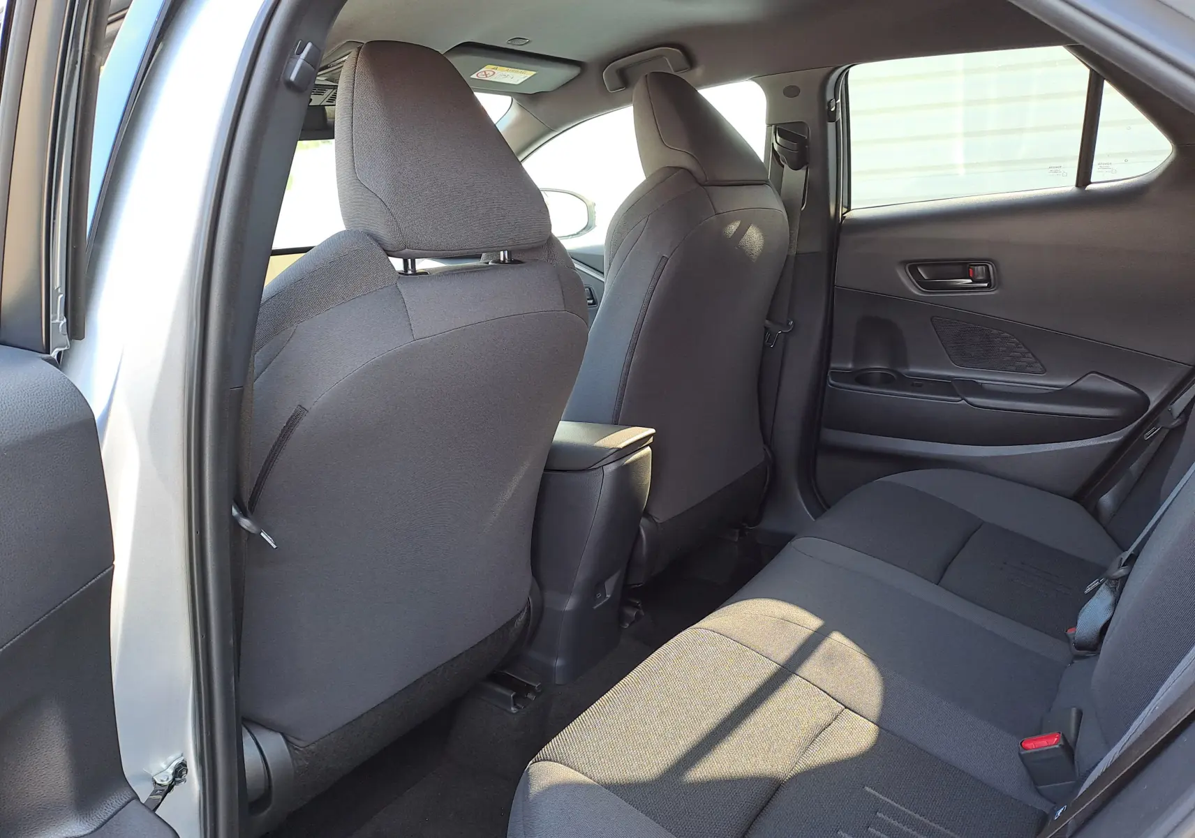 Vue intérieure sur la banquette arrière grise du Toyota C-HR II Style 1.8 Hybrid 2025, avec ceintures et appuie-têtes visibles.