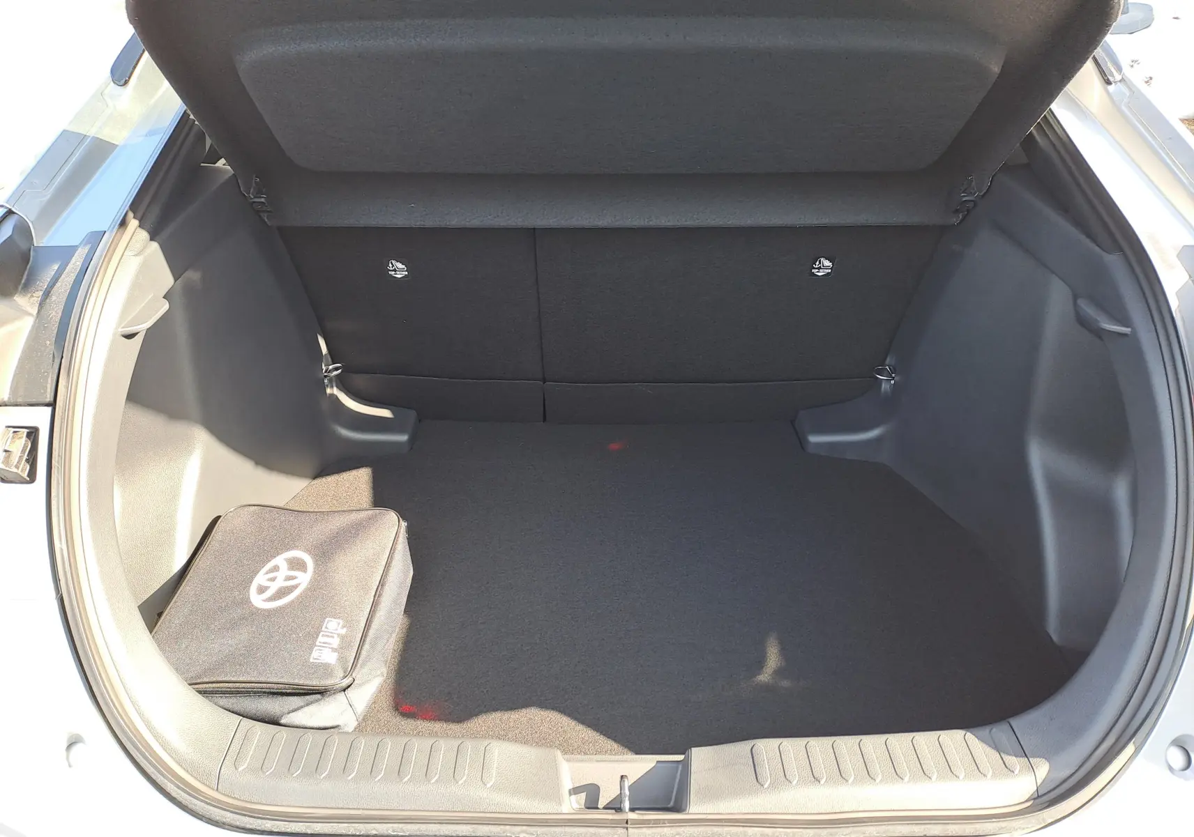 Coffre ouvert du Toyota C-HR gris minéral 2025 montrant le kit de réparation et les outils de secours rangés.
