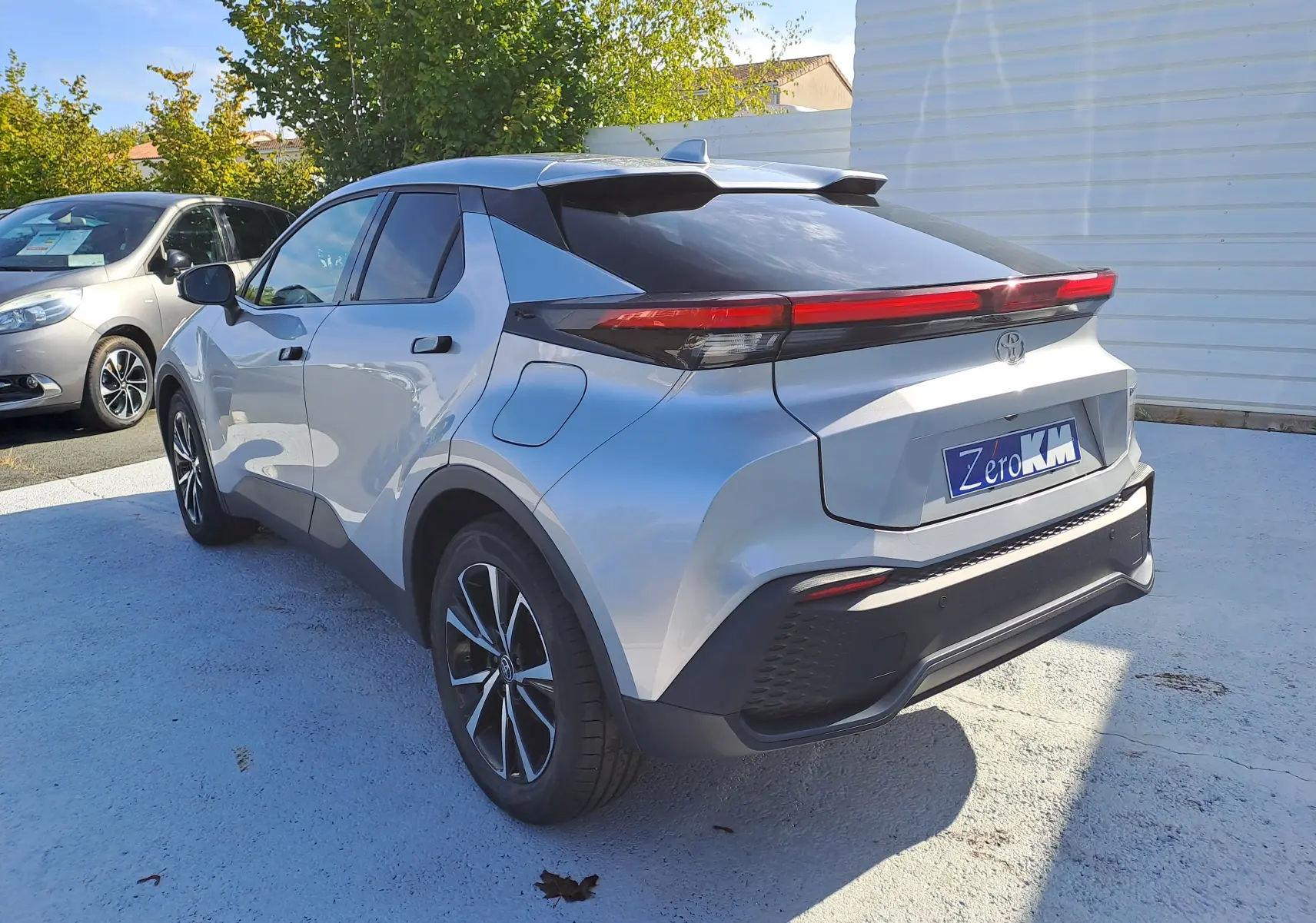 Vue arrière d'un Toyota C-HR gris minéral 2025 avec feux arrière horizontaux et plaque Zero KM visible.