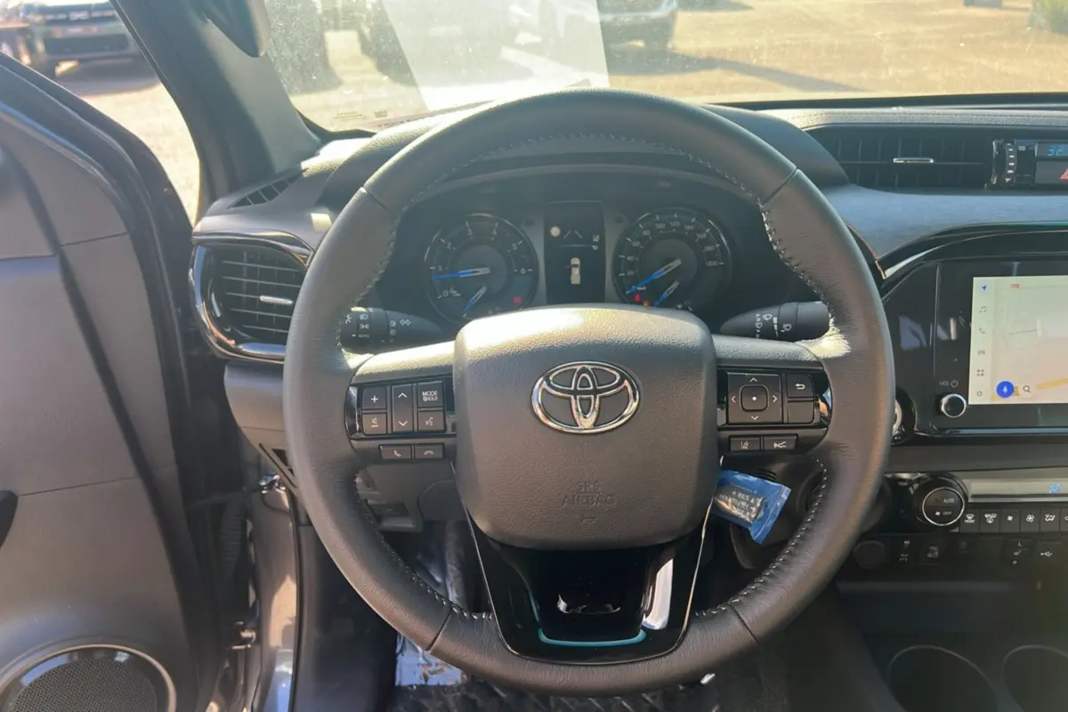 Vue intérieure centrée sur le volant du Toyota Hilux 2025, avec tableau de bord et écran tactile visibles.