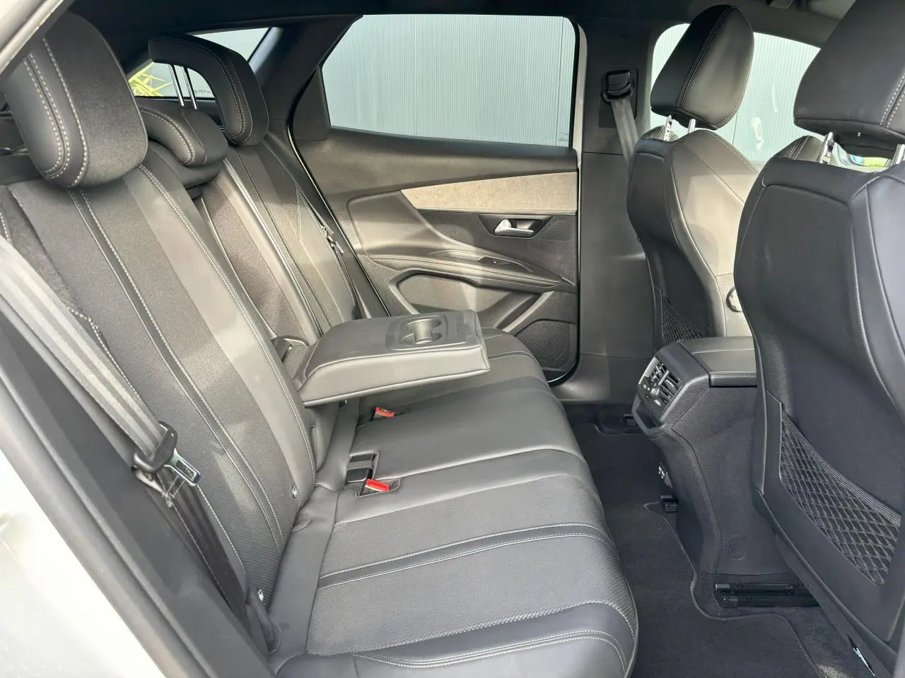 Vue intérieure côté gauche des sièges arrière du Peugeot 3008 2024 en cuir noir avec accoudoir central rabattable.