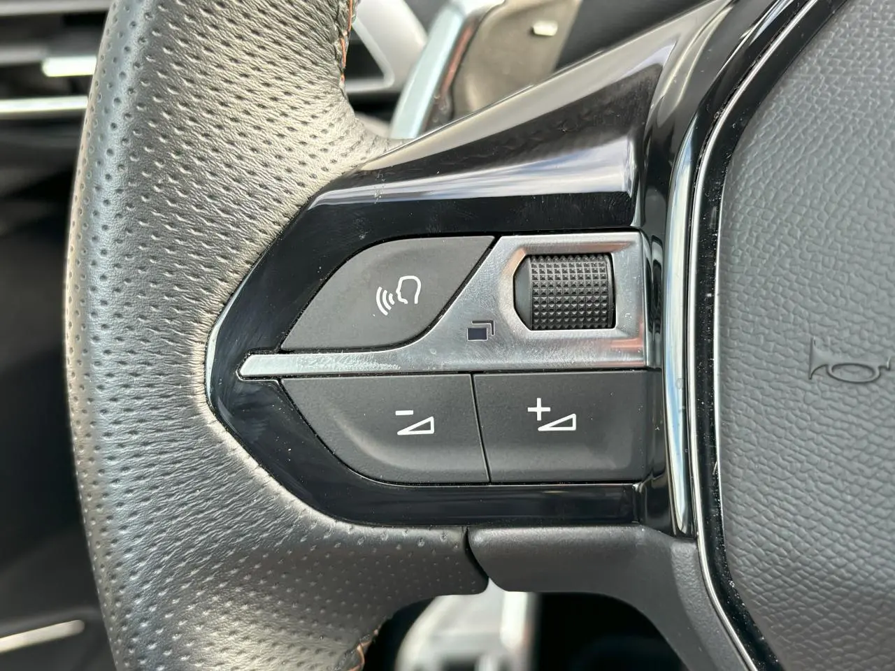 Gros plan sur les commandes gauche du volant cuir perforé du Peugeot 3008 2024 blanc nacré avec touches chromées.