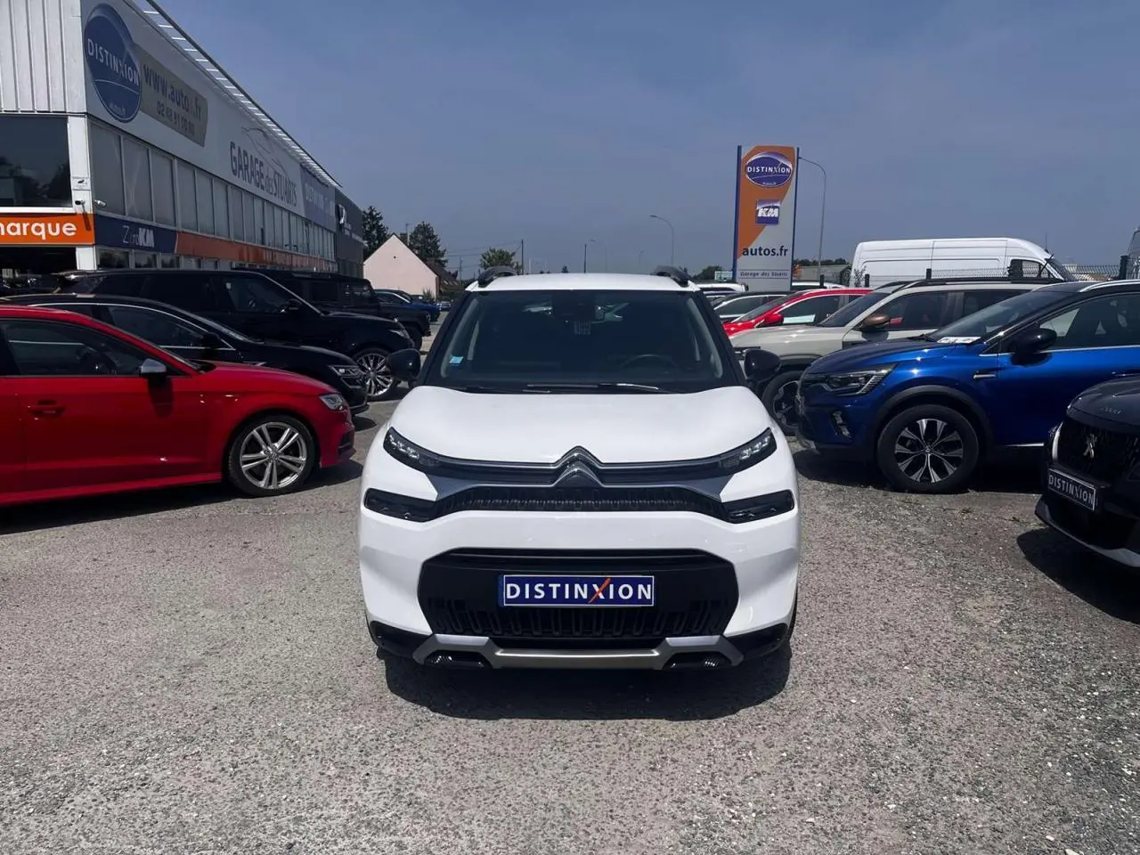 Vue avant d'un Citroën C3 Aircross blanc banquise avec calandre noire et barres de toit noires, stationné en extérieur.