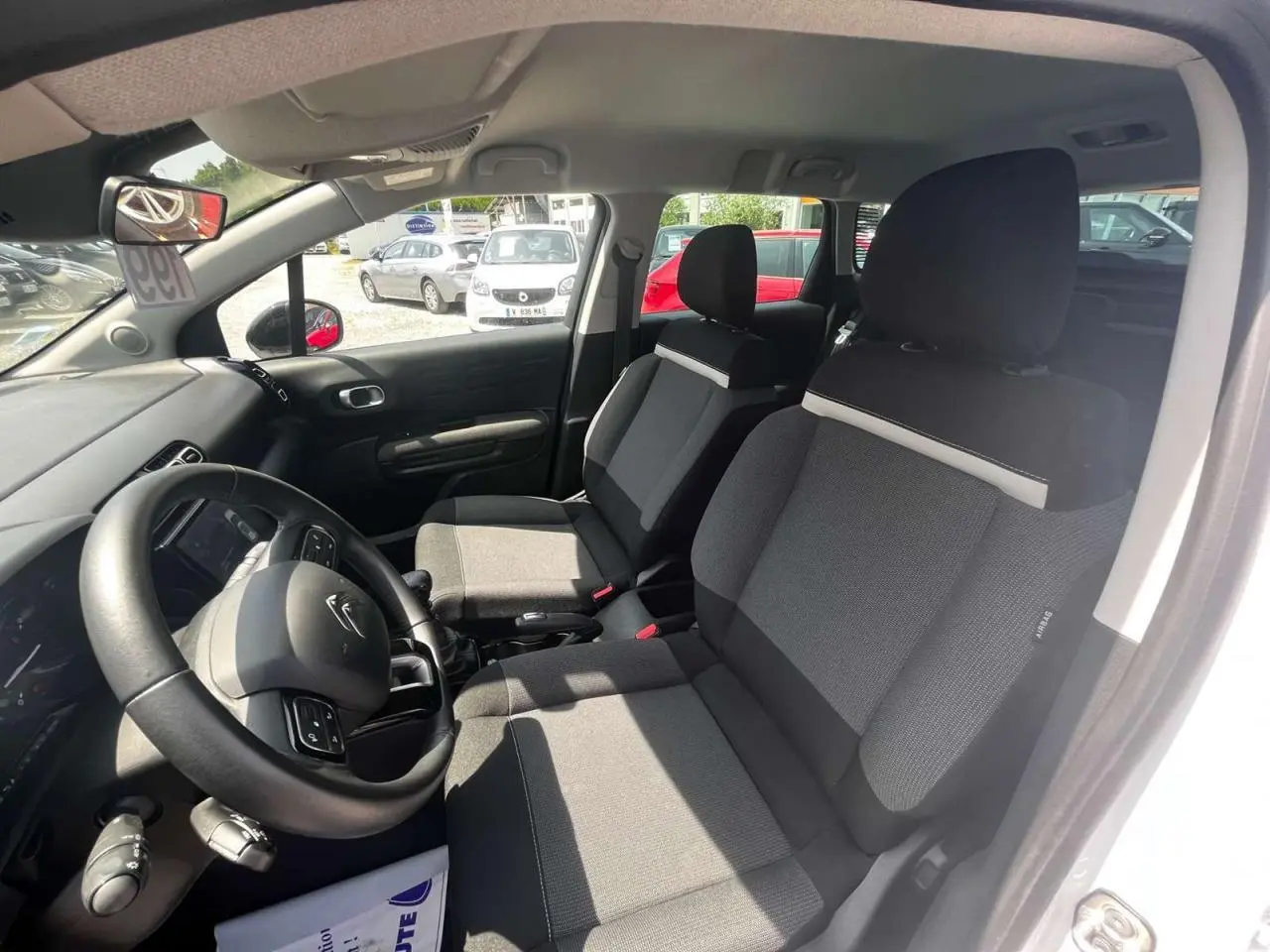 Intérieur avant du Citroën C3 Aircross blanc banquise 2023, sièges tissu gris et volant multifonction noir.