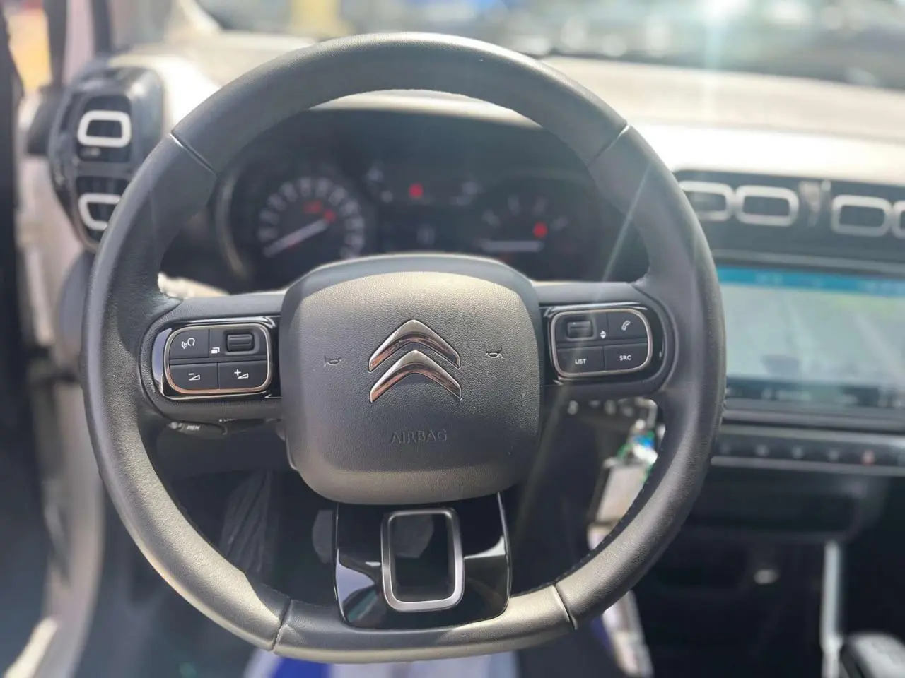 Vue rapprochée du volant noir de la Citroën C3 Aircross 2023 avec commandes intégrées et tableau de bord flou en arrière-plan.