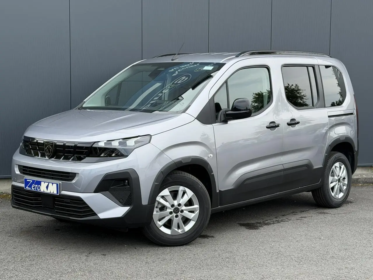 Peugeot Rifter gris acier vu en 3/4 avant droit, avec jantes alu 16 pouces et portes latérales coulissantes.