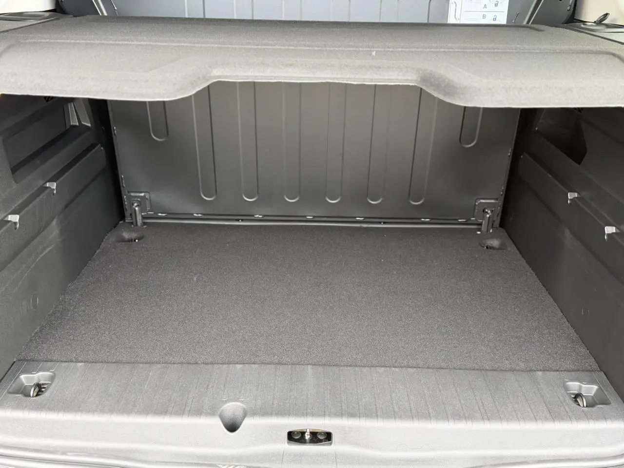 Coffre ouvert du Peugeot Rifter gris acier, vue arrière montrant l'espace de chargement et la tablette de séparation.