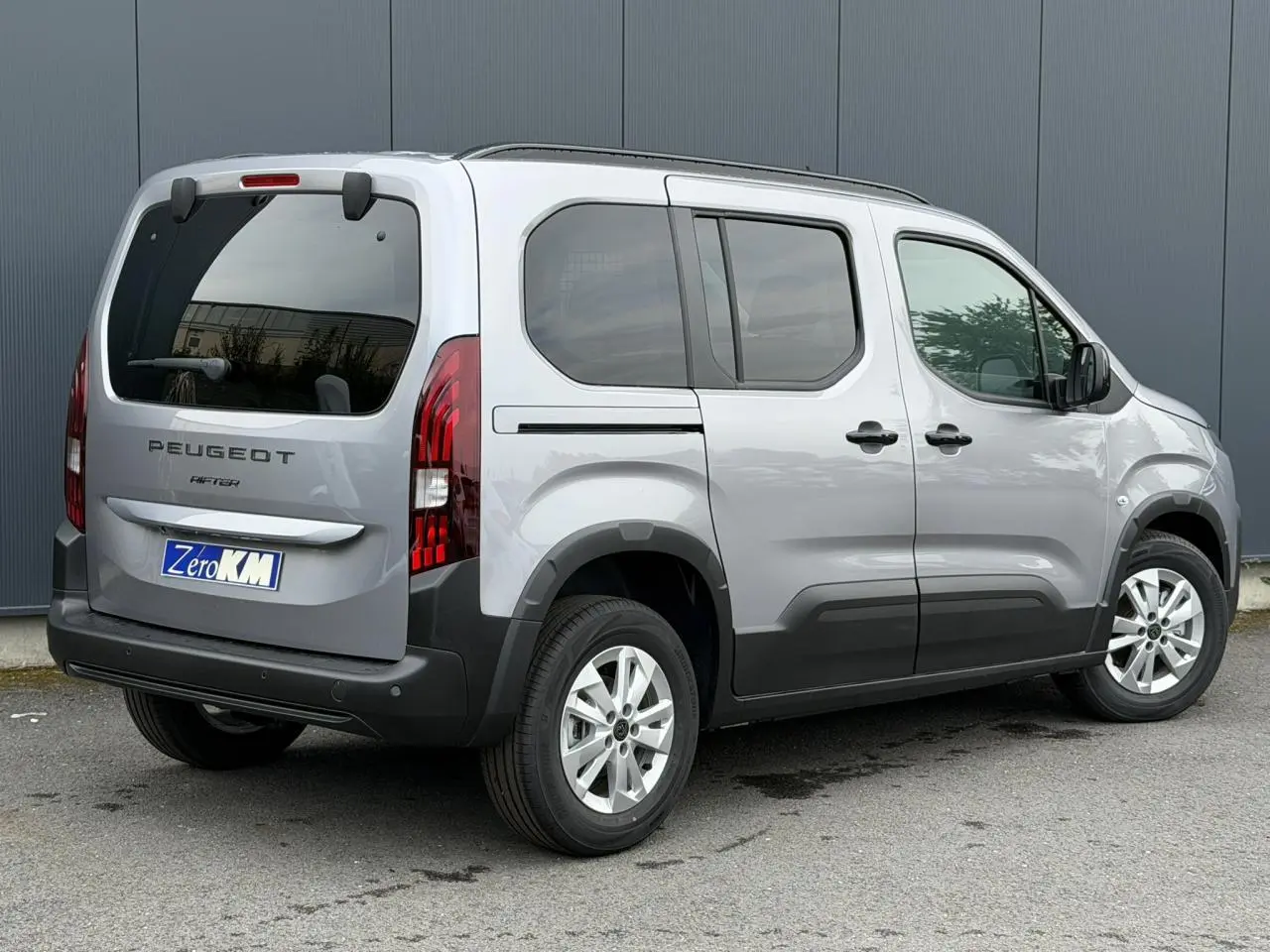 Vue 3/4 arrière droite du Peugeot Rifter gris acier 2026 avec vitres arrière surteintées et jantes alu 16 pouces.