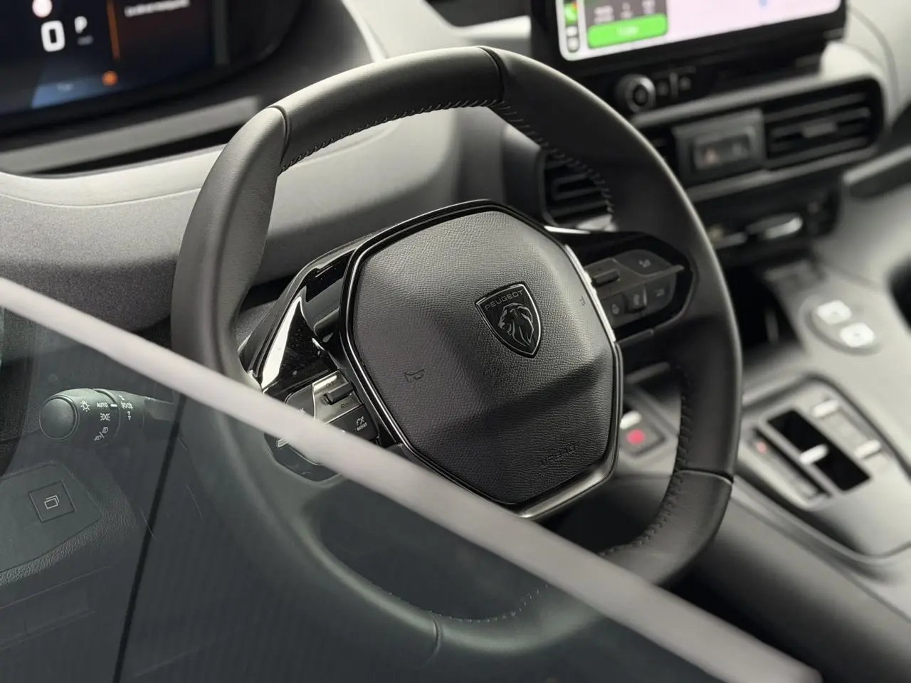 Vue rapprochée du volant cuir noir du Peugeot Rifter 2026 avec commandes intégrées et tableau de bord numérique partiel.
