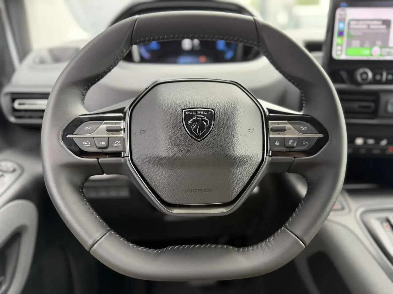 Vue rapprochée du volant cuir multifonction noir du Peugeot Rifter 2026 avec logo lion et commandes intégrées.