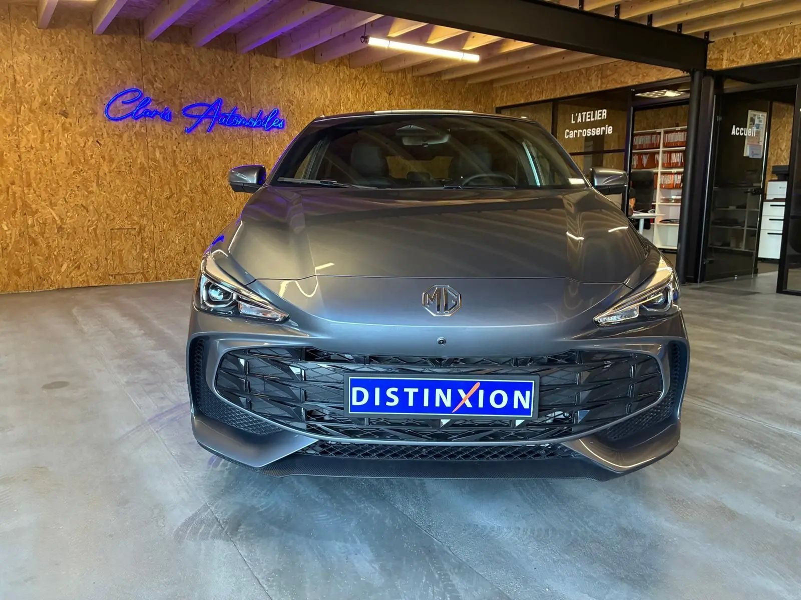 Vue de face d'une MG3 1.5 HYBRID+ 195 LUXURY noire, avec calandre large et phares LED allumés en intérieur showroom.