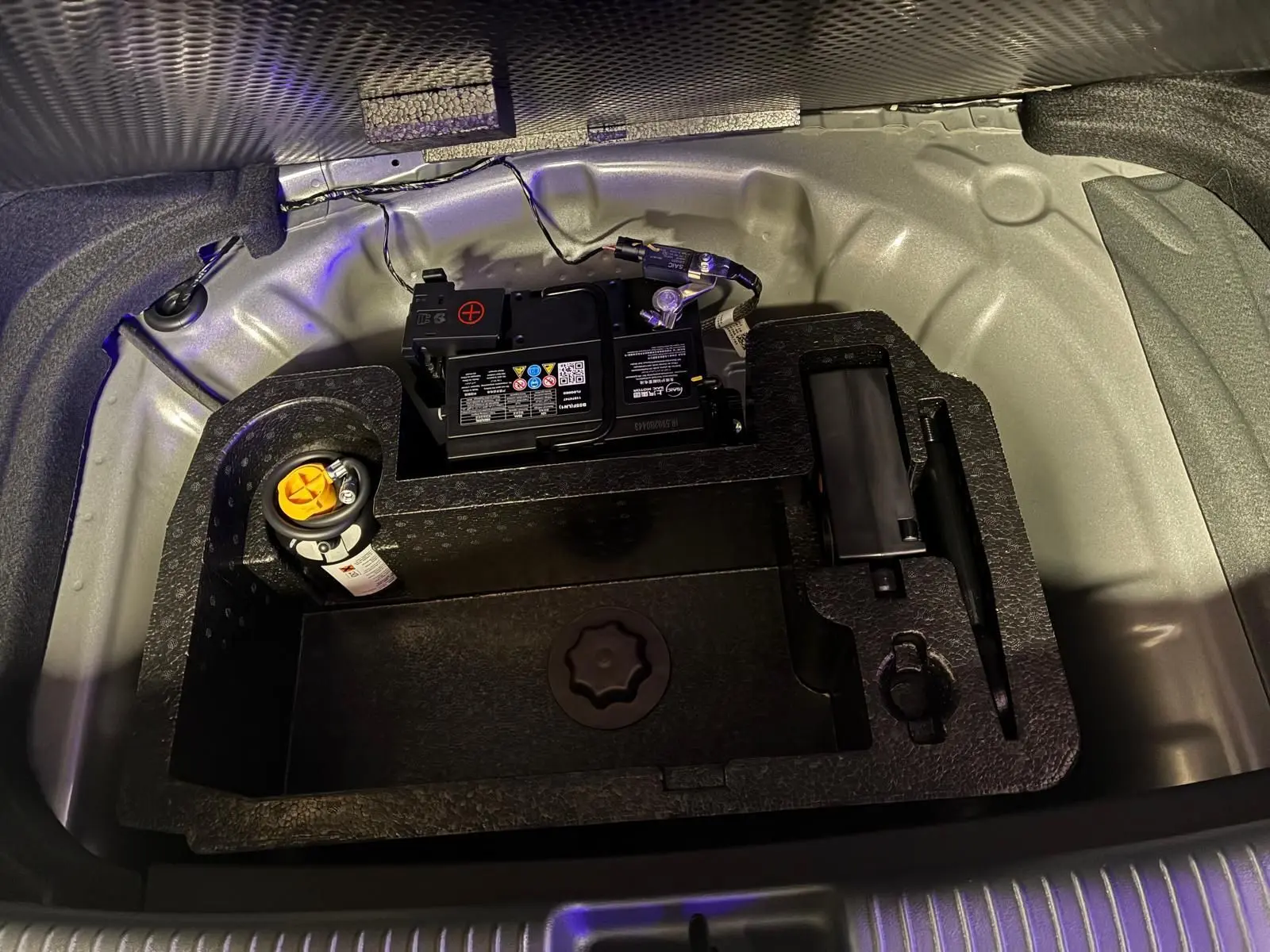 Vue rapprochée du compartiment batterie et outils sous le coffre d'une MG3 1.5 HYBRID+ 195 LUXURY noire, année 2026.